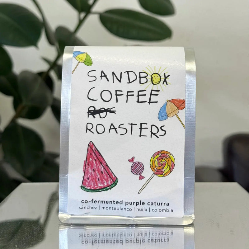 Sandbox Coffee Roasters packaging with colorful illustrations on a reflective surface.