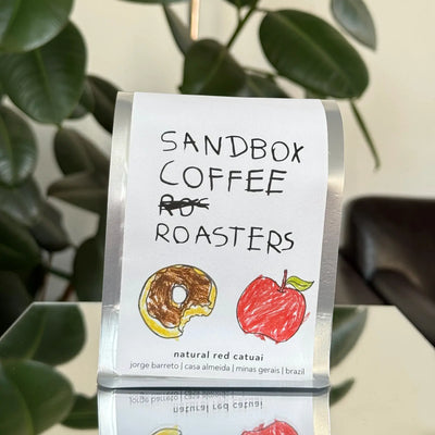 Sandbox Coffee Roasters coffee bag with illustrations of a donut and an apple on a stand.