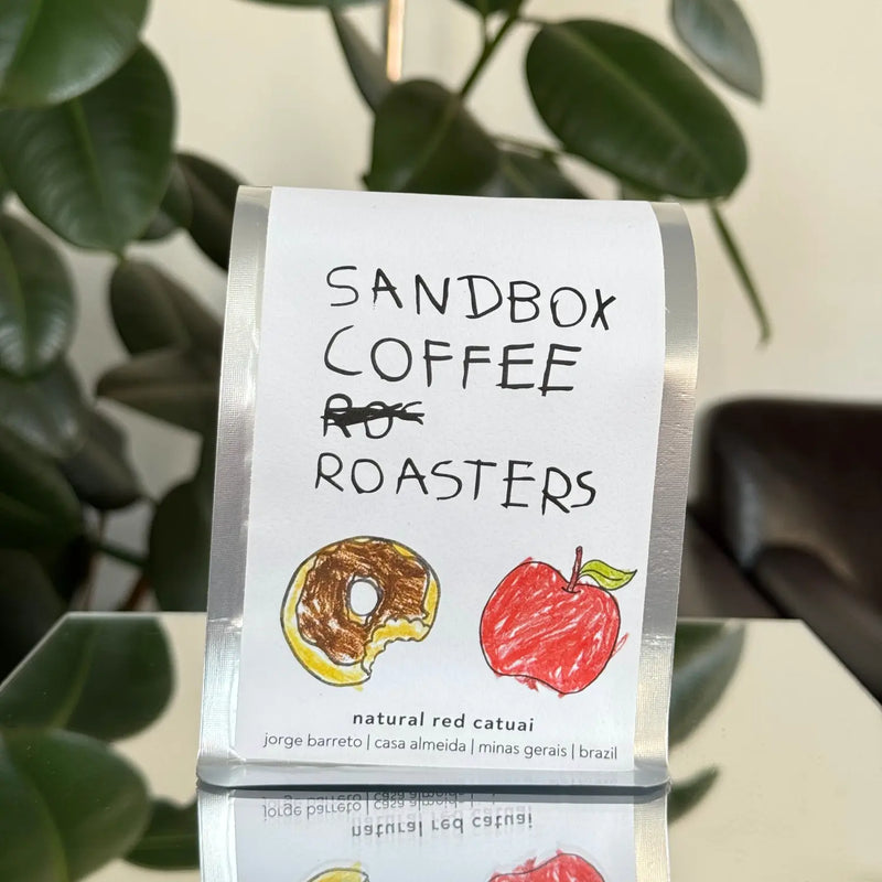 Sandbox Coffee Roasters coffee bag with illustrations of a donut and an apple on a stand.