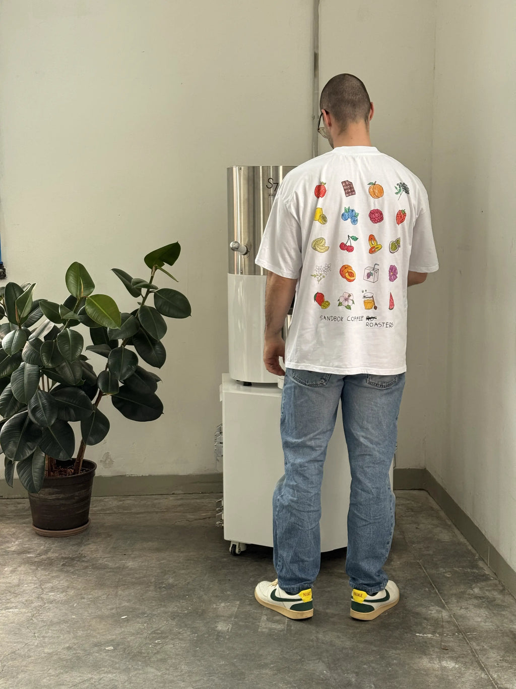 Man in jeans and graphic coffee t-shirt standing by coffee roaster in a minimalist room