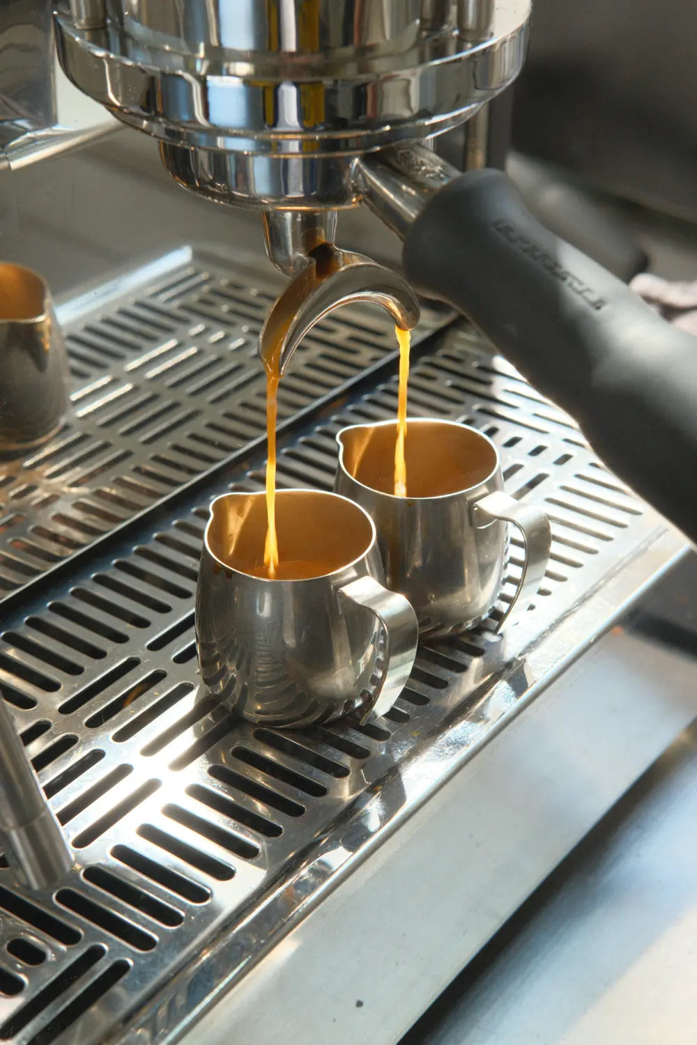 Espresso machine pouring coffee into two metal cups.