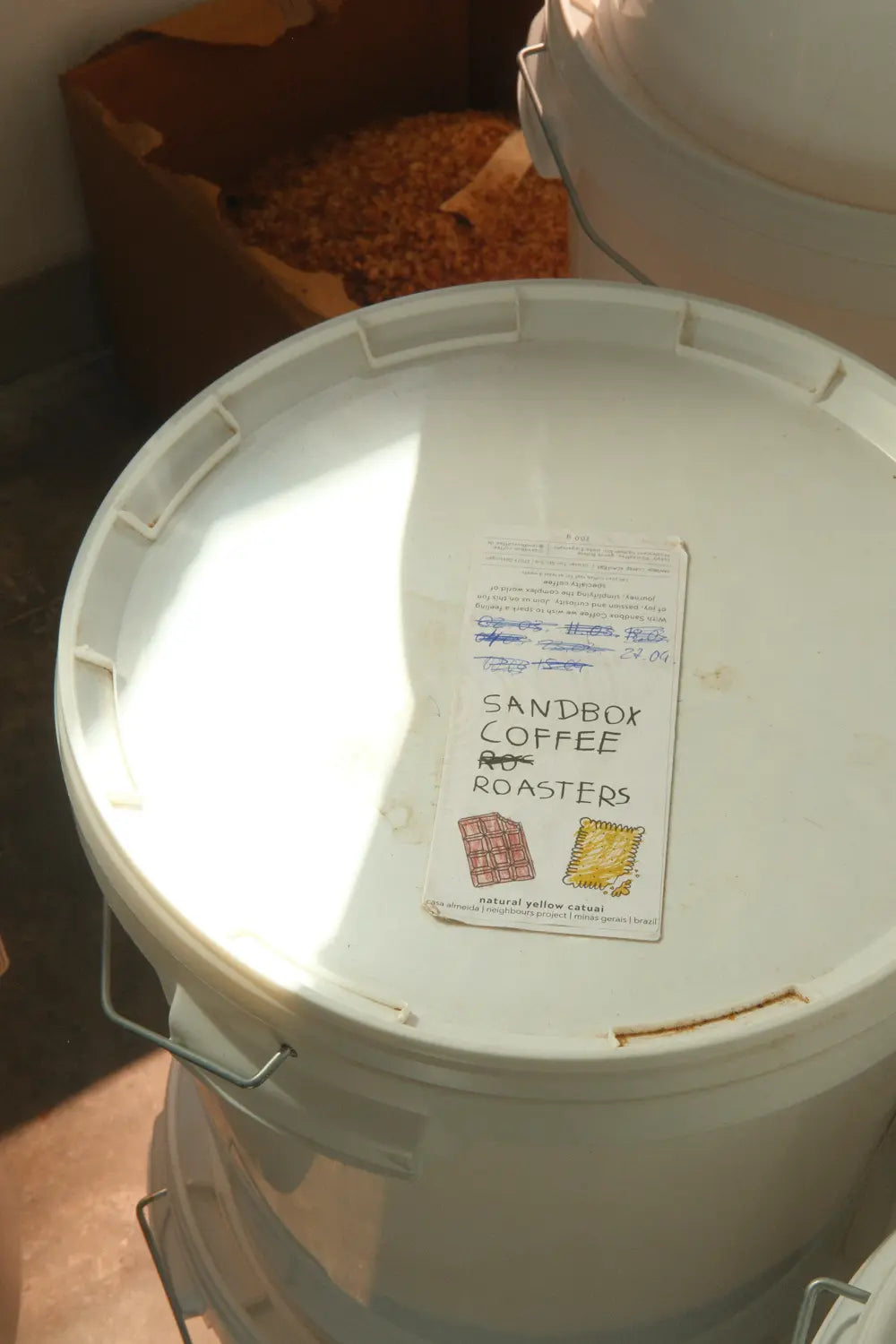 White bucket with a label on top, featuring 'Sandbox Coffee Roasters'.