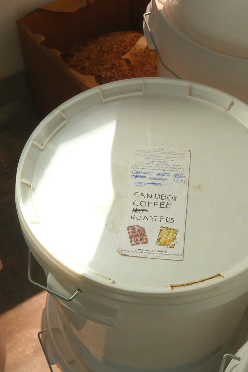 White bucket with a label on top, featuring 'Sandbox Coffee Roasters'.